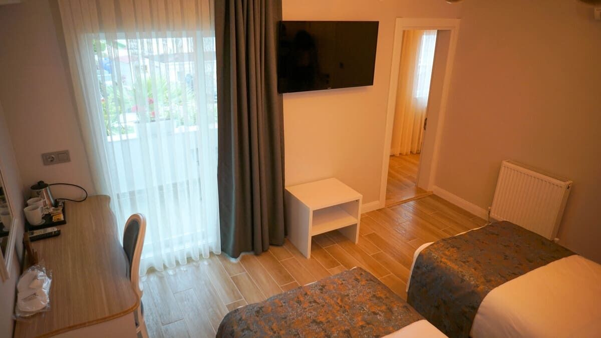 A hotel room with a bed, a desk, a TV mounted on the wall, and a window with curtains.