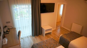 A hotel room with a bed, a desk, a TV mounted on the wall, and a window with curtains.