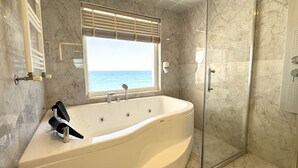 A bathroom with a bathtub, a glass-enclosed shower, and a window with a view of the sea. - Beyaz Ev Hotel Restaurant (Sinop)