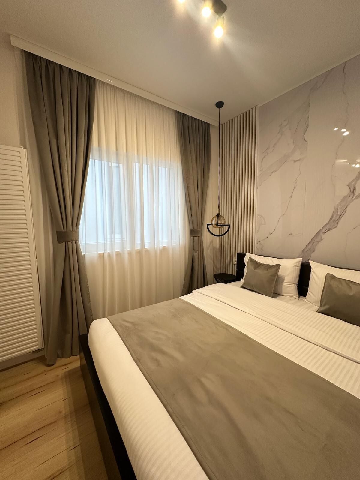 A modern bedroom with a large bed, curtains, a marble wall, and a hanging light fixture.