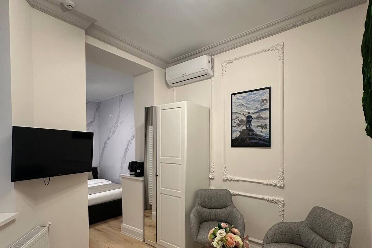 A modern living room with a flat-screen TV, a grey armchair, a black coffee table with flowers, a white door, and a framed picture on the wall.
