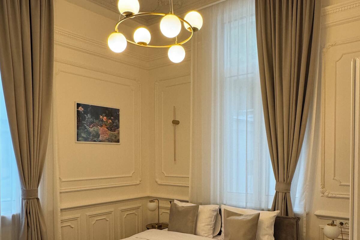 A spacious bedroom with a large bed, a modern chandelier, and a painting on the wall.