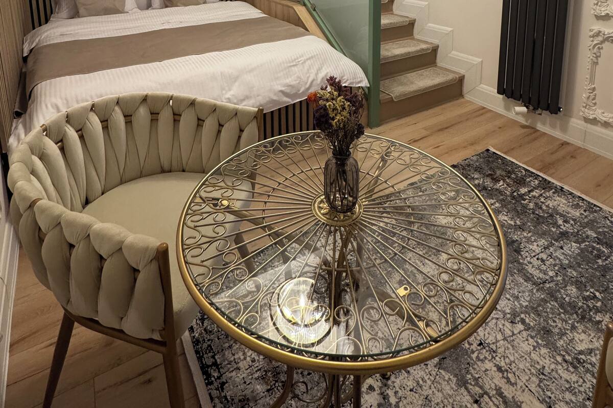 A modern hotel room with a large bed, a curved seating area, a round table with a vase, and a staircase.