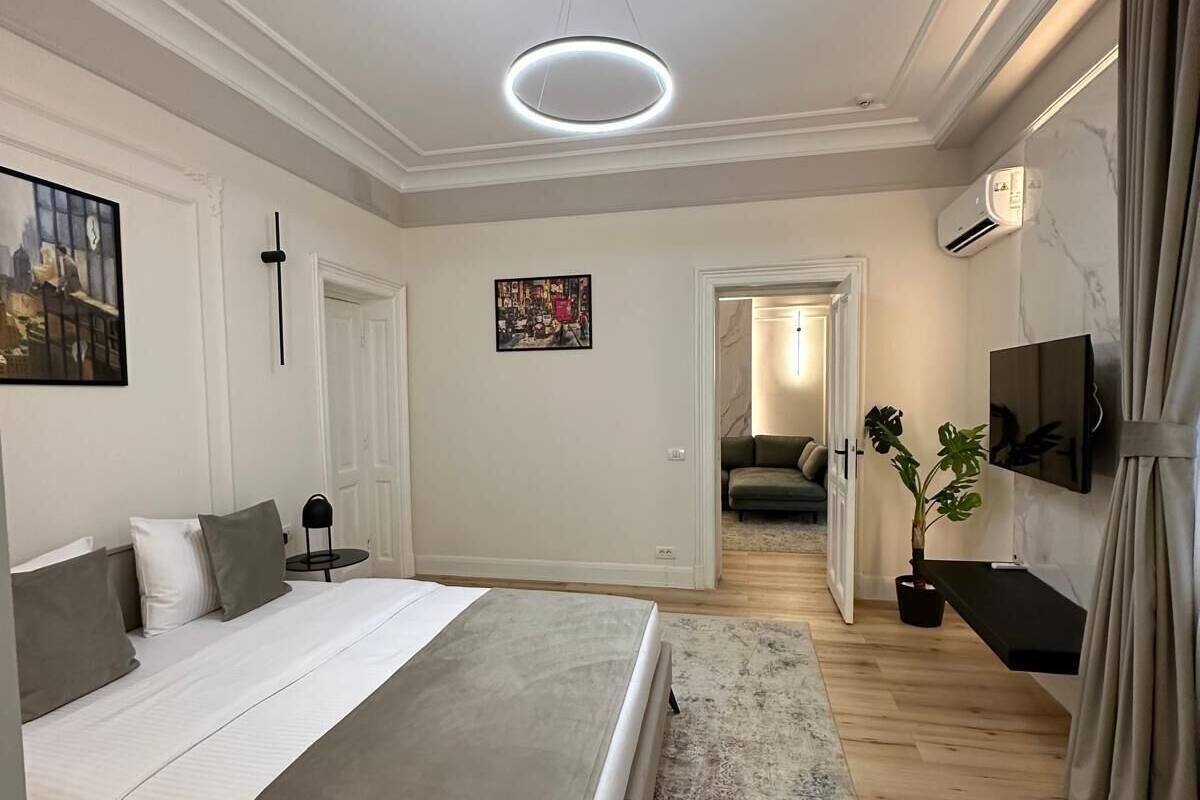 A modern bedroom with a large bed, a bedside table, a wall-mounted TV, and a ceiling light.