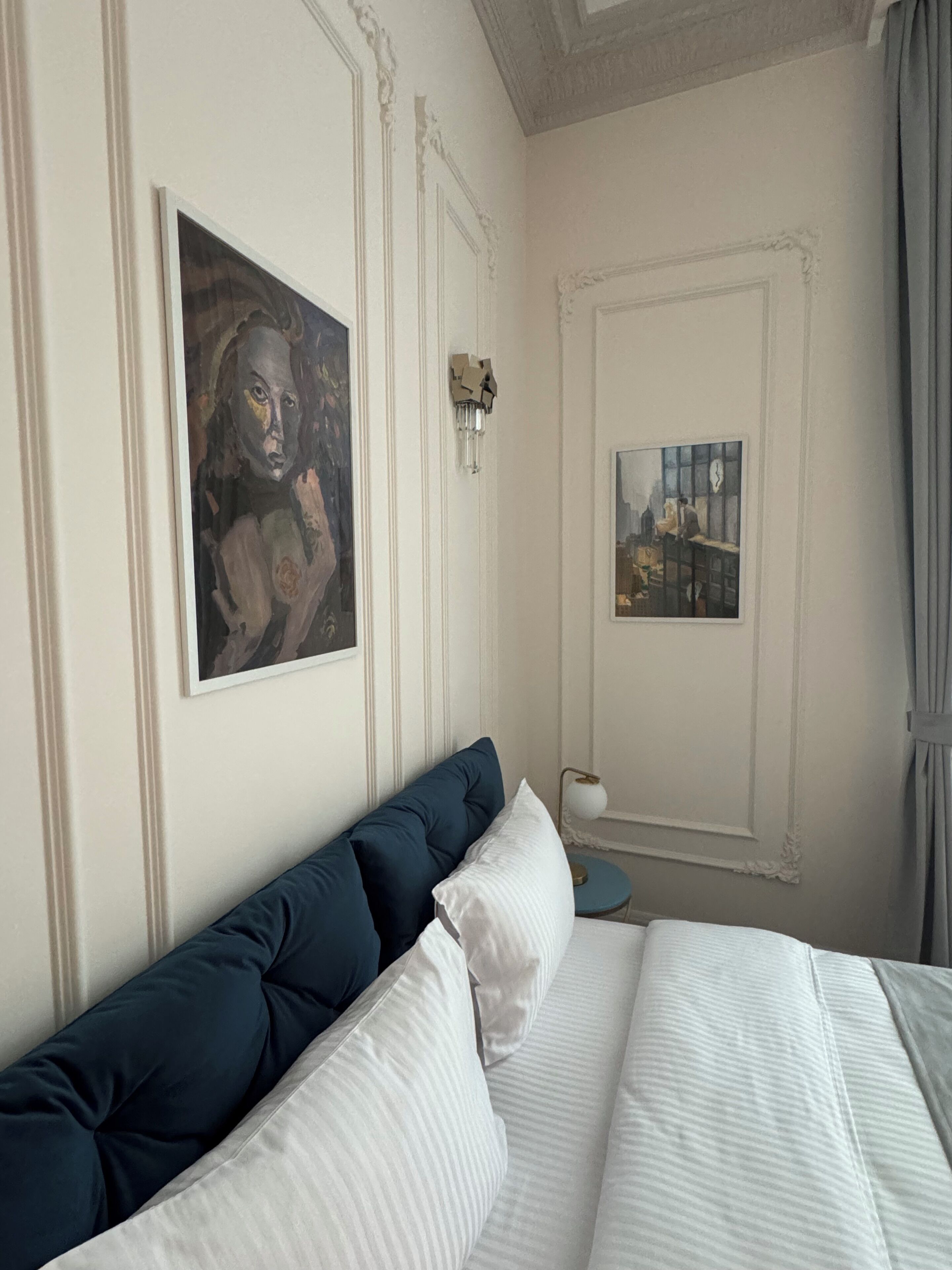Une chambre à coucher avec un lit, des oreillers, une lampe fixée au mur et deux œuvres d’art encadrées.