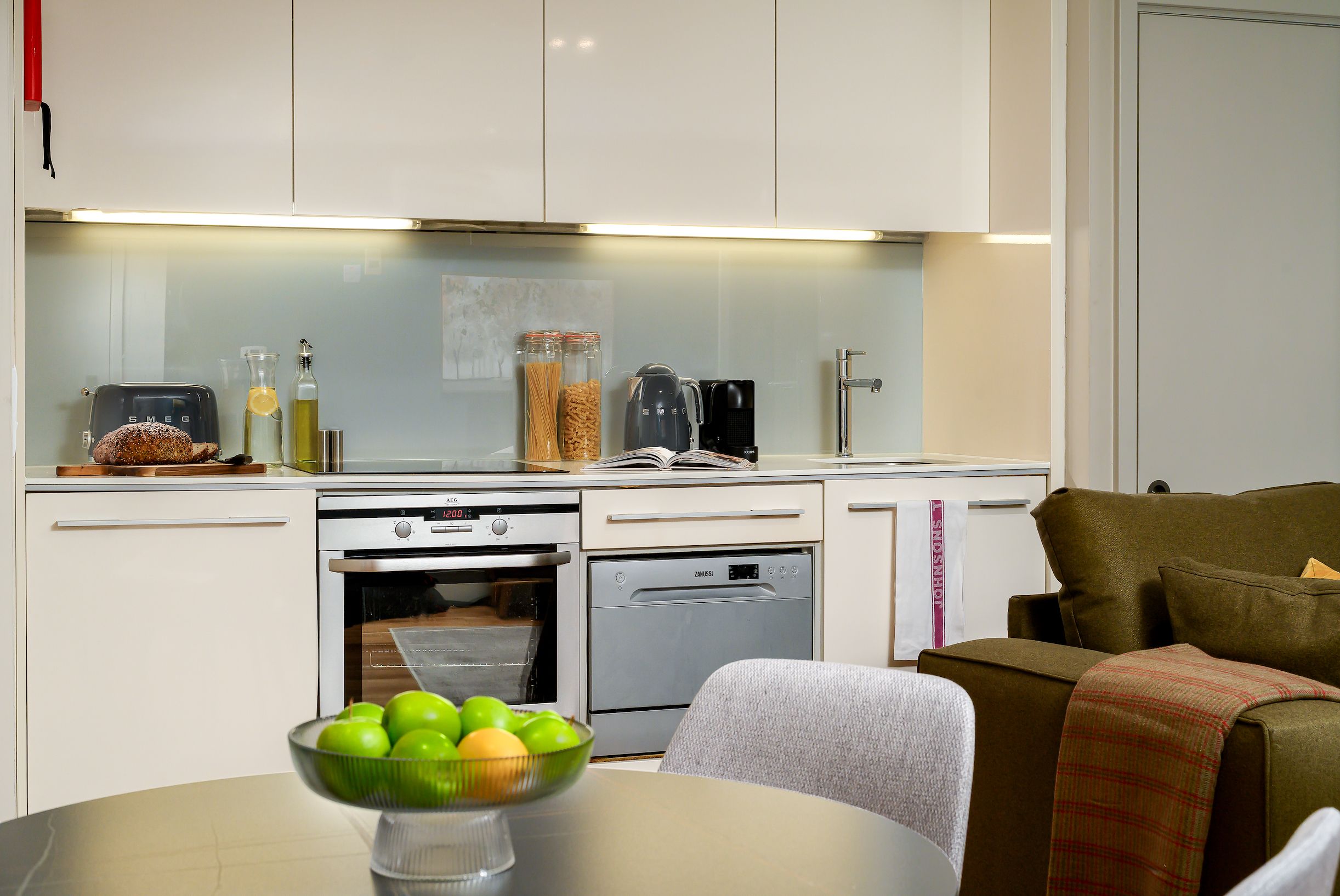 A modern kitchen with white cabinetry, a built-in oven, and a dining area with a table set for a meal.