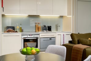 Una cocina moderna con armarios blancos, horno integrado y comedor con mesa lista para una comida.