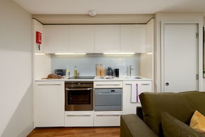 Una cocina compacta con armarios blancos, horno empotrado, lavavajillas y cafetera.
