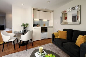 A modern living room with a black sofa, a coffee table, and a dining area with two chairs.