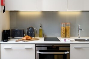 A modern kitchen with a built-in oven, a coffee maker, a kettle, and jars of pasta.