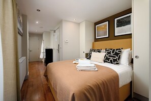 Ein Hotelzimmer mit Bett, Nachttisch, Heizkörper, Tür und Flur.