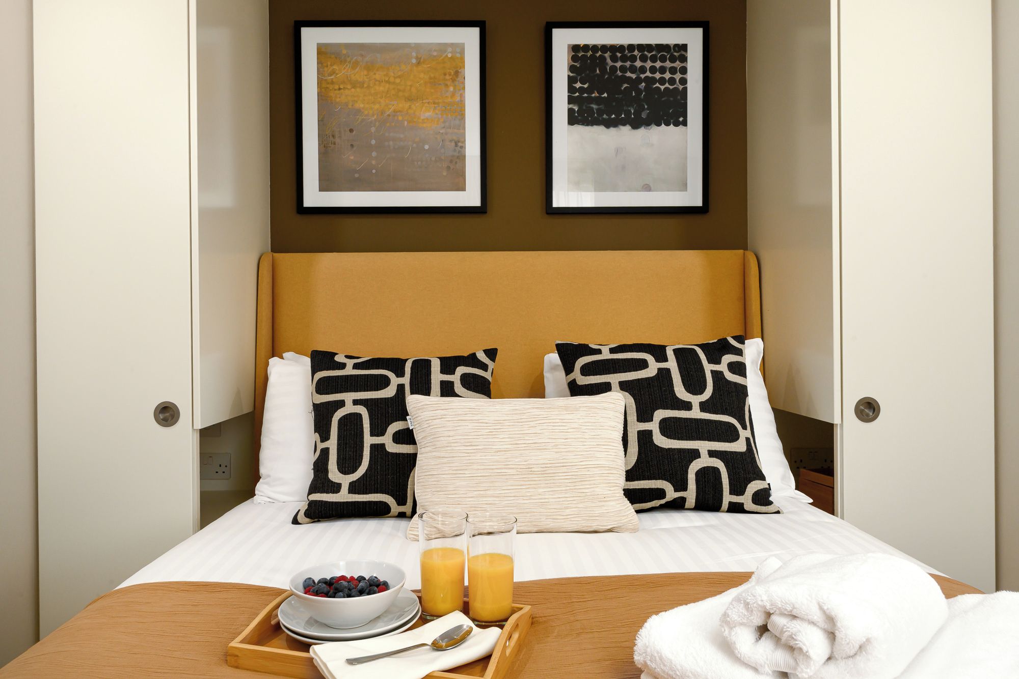 Una habitación de hotel con una cama, una bandeja de desayuno y dos obras de arte enmarcadas en la pared.