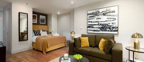 A modern hotel room with a bed, a sofa, a coffee table, and a painting on the wall.