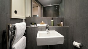 A modern bathroom with a white sink, dark tiled walls, and a mirror above the sink.