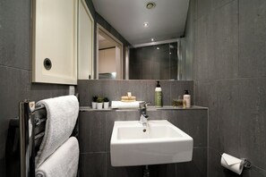 Un baño moderno con un lavamanos blanco, paredes de azulejos oscuros y un espejo sobre el lavamanos.
