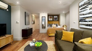 A modern living room with a sofa, a coffee table with a bowl of fruit, a television, and a bed with a headboard in the background.
