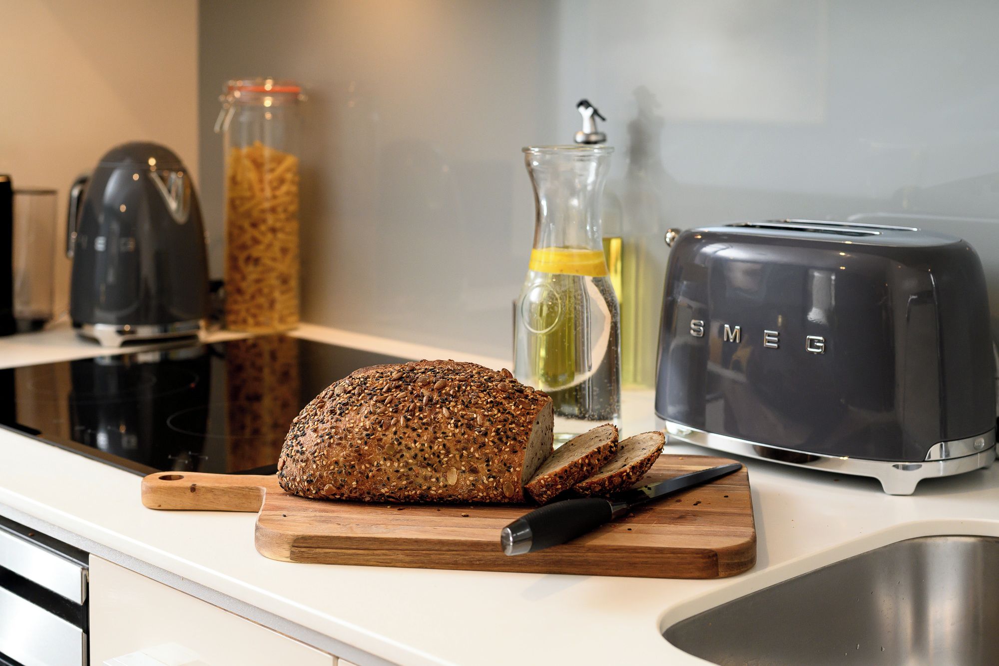 Un plan de travail de cuisine avec un pain aux graines, un grille-pain, un couteau et une planche à découper.