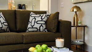 Una sala de estar con un sofá, un cuenco de manzanas verdes, una vela y una mesita con una lámpara y un florero.