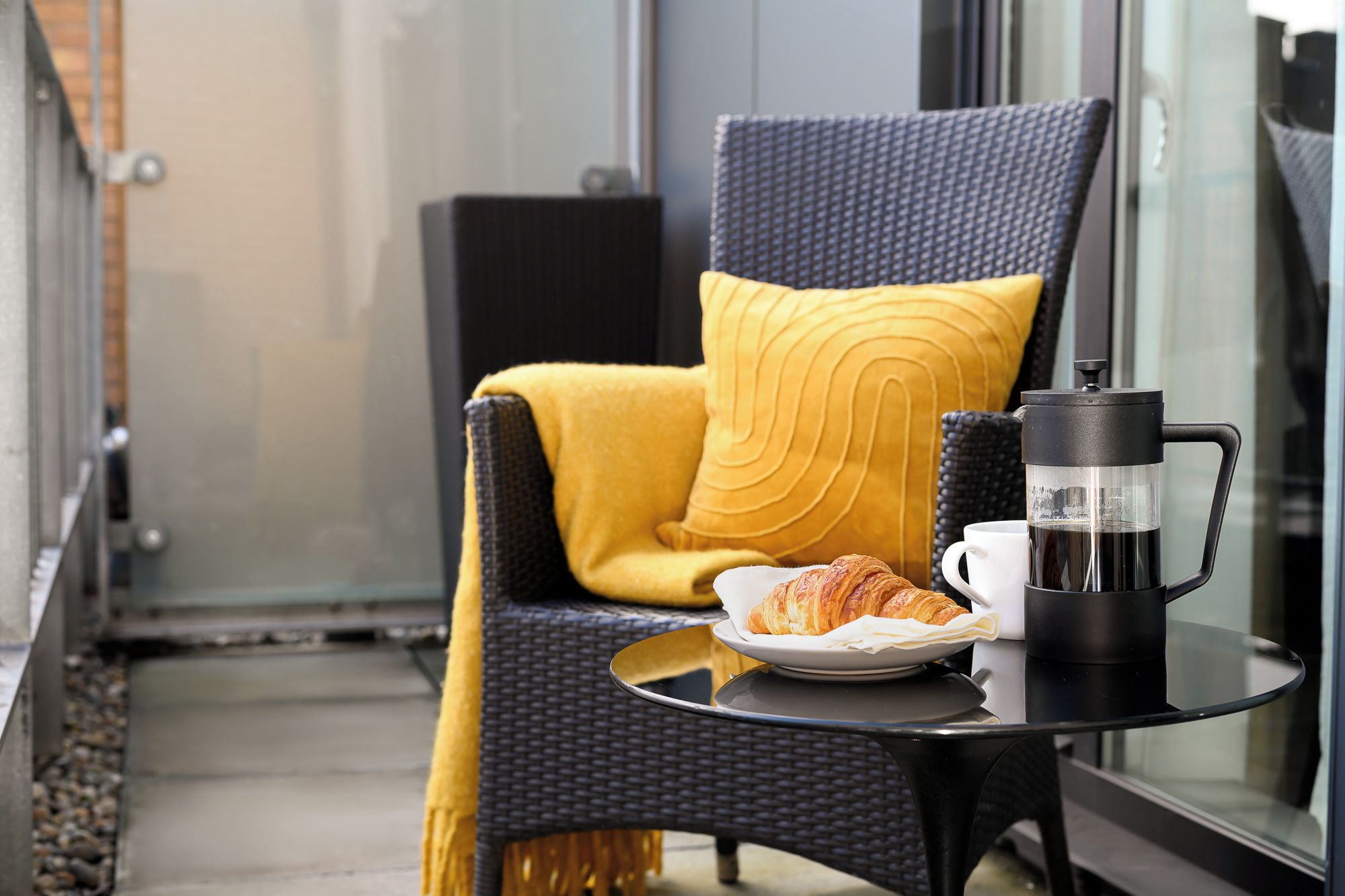 Ein Balkon mit einem Stuhl, einer Kaffeemaschine, einem Teller mit Croissants und einer Tasse.