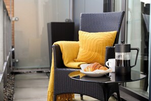 A balcony with a chair, a coffee maker, a plate with croissants, and a cup.