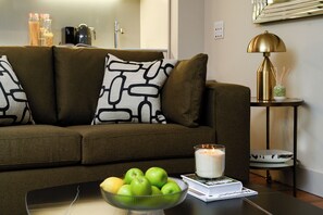 A living room with a sofa, a coffee table with a bowl of apples, a candle, and a lamp on a side table.