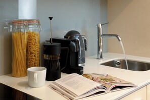 A kitchen counter with jars of pasta, a coffee maker, a kettle, a sink, and a cookbook.