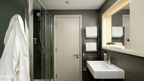 A modern bathroom with a glass shower enclosure, a white sink, and a towel rack with multiple towels.