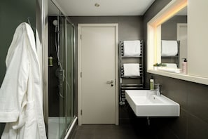 Un baño moderno con ducha de vidrio, lavamanos blanco y un perchero para toallas.