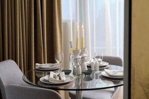 A dining table set with plates, glasses, and candles, with a view of curtains and a window in the background.