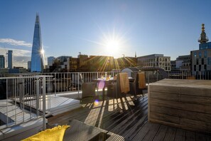 Una terraza en la azotea con vistas al horizonte urbano, incluyendo un rascacielos destacado.