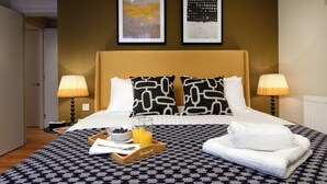 A hotel room with a bed, two bedside lamps, a tray with breakfast, and two framed artworks on the wall.