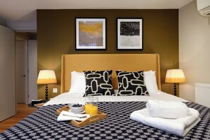 Habitación de hotel con una cama, dos lámparas de noche, una obra de arte enmarcada sobre la cama y una bandeja con alimentos para el desayuno.