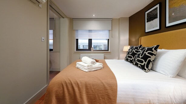 A hotel room with a bed, a window, a radiator, and a towel rack.