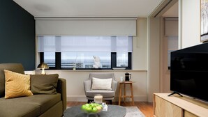 A modern living room with a sofa, a chair, a coffee table with apples, a TV, and a window with blinds.