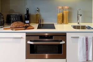 Une cuisine équipée d’un grille-pain, de pain, d’une bouteille, de pots de sauce pour pâtes et d’un évier.
