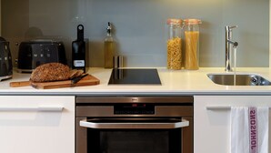 A modern kitchen with a built-in oven, a toaster, a bread loaf, and jars of pasta.