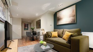 A modern living room with a sofa, a coffee table, and a TV. There is a dining area with chairs and a table.