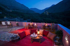 A rooftop terrace with a red carpet, seating area, tables with candles, and a mountainous backdrop. - Atlas toubkal viow  (Asni)