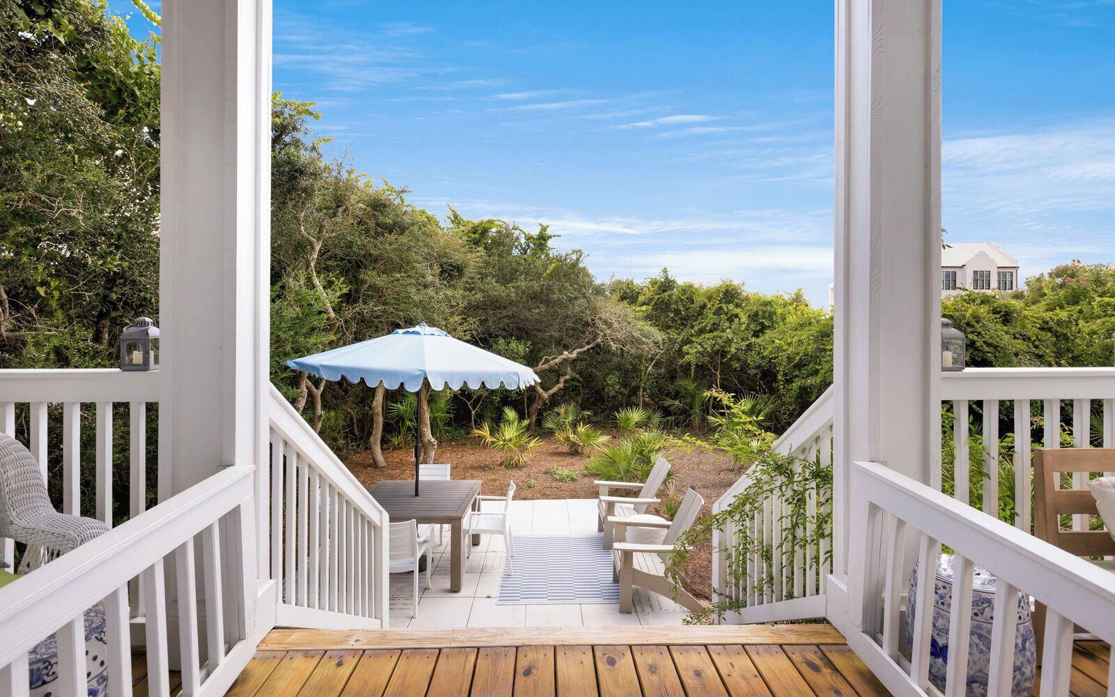 A wooden deck with a table and chairs, a blue umbrella, and a view of a lush garden.