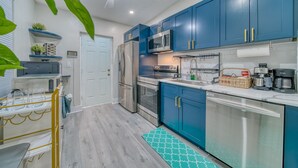 A modern kitchen with blue cabinets, stainless steel appliances, and a teal patterned rug.