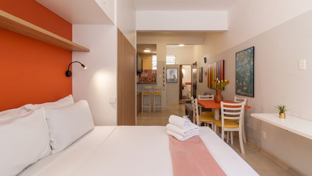 Habitación de hotel con una cama, un escritorio y una silla. Hay un cuadro en la pared y una planta en el escritorio.