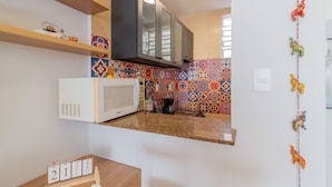 Una cocina con microondas, estantes de madera, un colorido salpicadero de azulejos y un calendario.