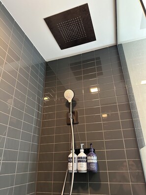 A shower area with a rain showerhead, a handheld showerhead, and three bottles of shampoo, conditioner, and body wash.