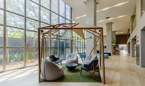 A modern indoor space with large windows, a wooden structure, and seating areas.