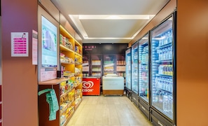 A grocery store aisle with shelves stocked with various products, a refrigerated section, and a red kiosk.