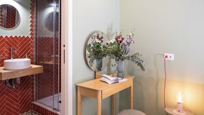 Un baño con espejo, lavamanos y una mesita con un florero.