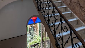 Una escalera con barandillas de hierro ornamentadas y vista a un jardín a través de una ventana.