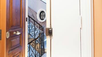 Una puerta de madera con un ojo de cerradura y un pomo de latón, que da a una escalera con barandilla de hierro forjado negro y un ventanal circular.