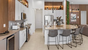 Una cocina moderna con armarios blancos, una isla central con taburetes de bar, electrodomésticos de acero inoxidable e iluminación empotrada.