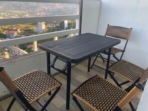 Un balcón con una mesa y cuatro sillas de mimbre, con vistas a un paisaje urbano.